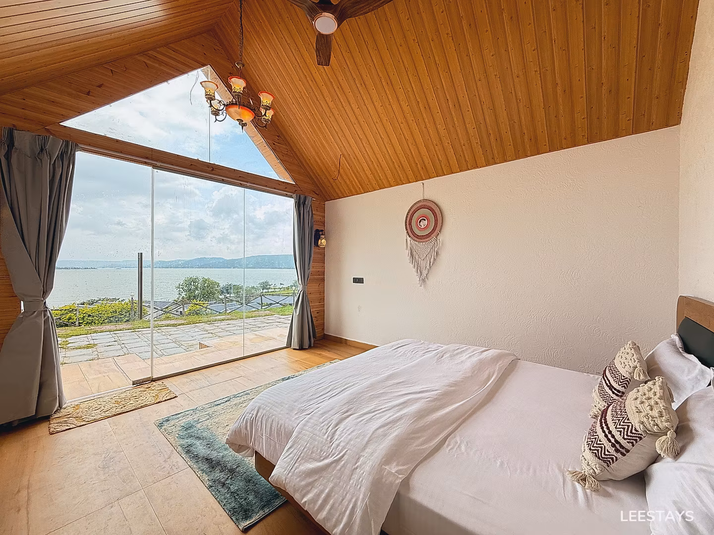 Bed with white linens facing a large window overlooking a lake and green landscape.