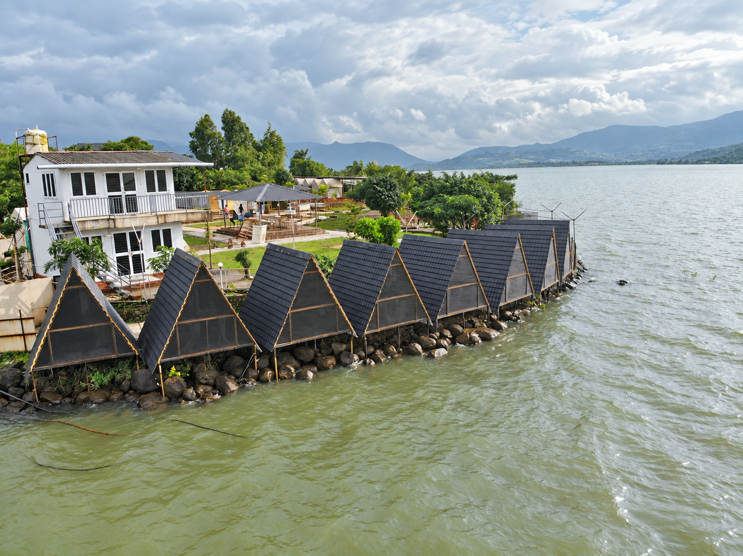 Aerial close view of NightVibe triangle cabins lined along the Pawna Lake shore.