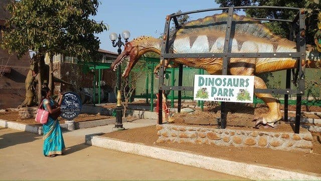 A life-sized dinosaur model displayed at Dinosaurs Park in Lonavala with a visitor in traditional attire.