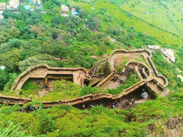 Aerial view of ancient stone fortifications surrounded by lush green hills and pathways.