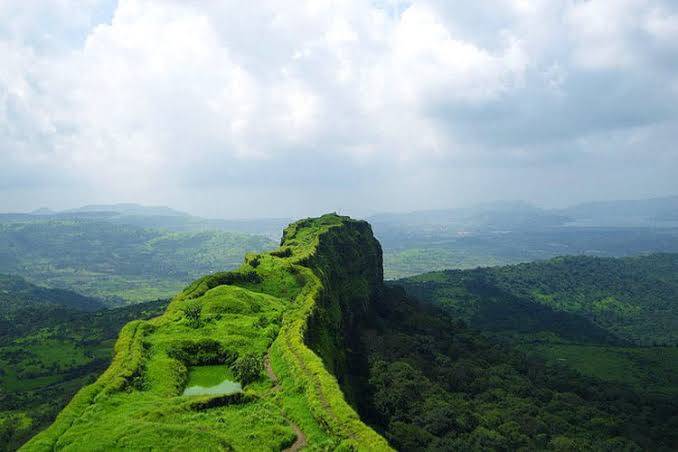 A panoramic view of a lush green mountain ridge with a winding path and cloudy sky in the background.