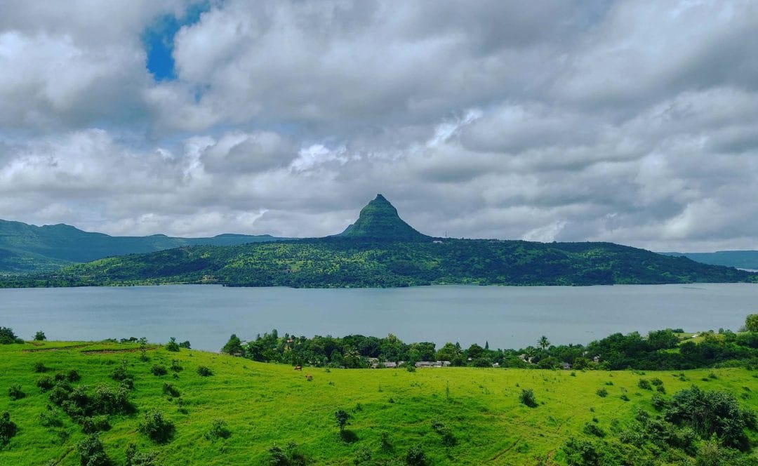 View of Pawna Lake surrounded by green hills under a cloudy sky near Lonavala, India.