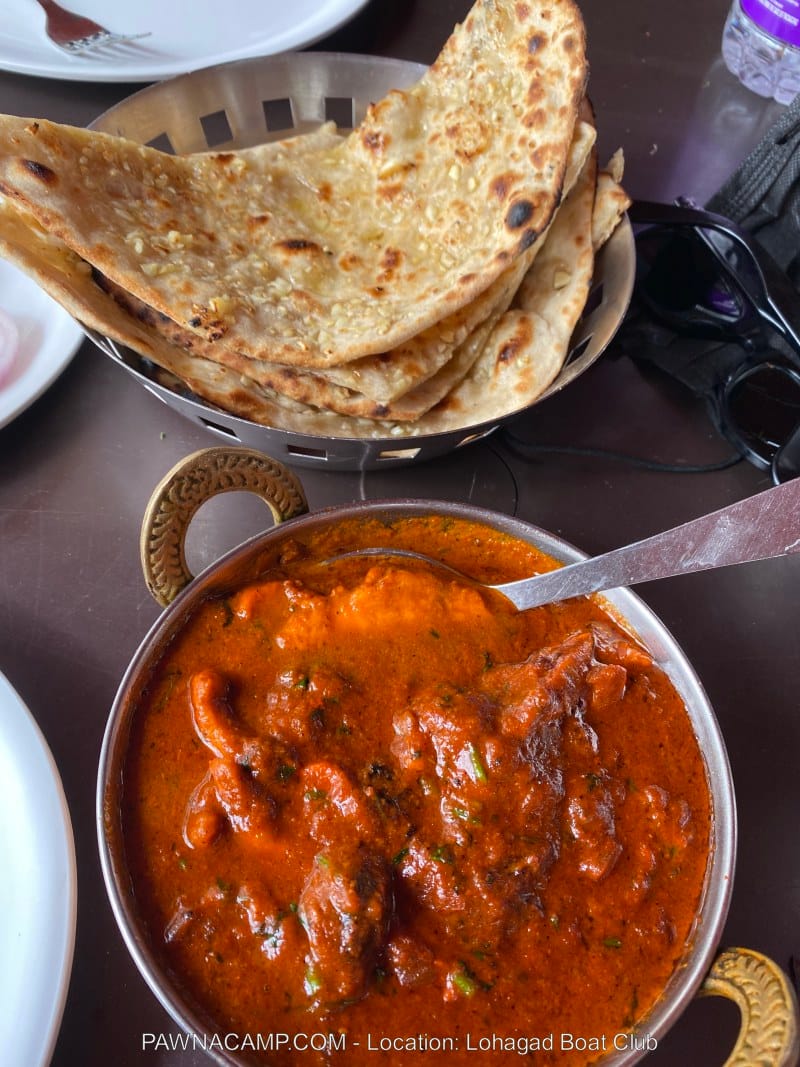 A bowl of chicken curry in a rich red sauce served with multiple pieces of roti on a plate.