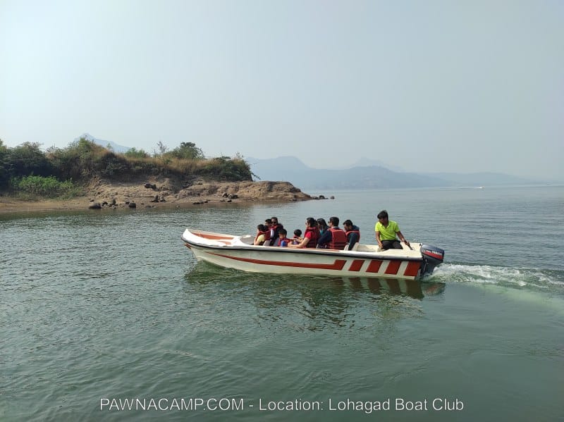 A speedboat carrying several passengers navigating through the waters of Pawna Lake near Lohagad Boat Club.