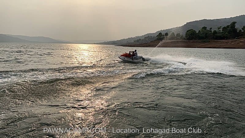 A jet ski navigating through the waters of Pawna Lake, creating waves and spray in the sunlight.