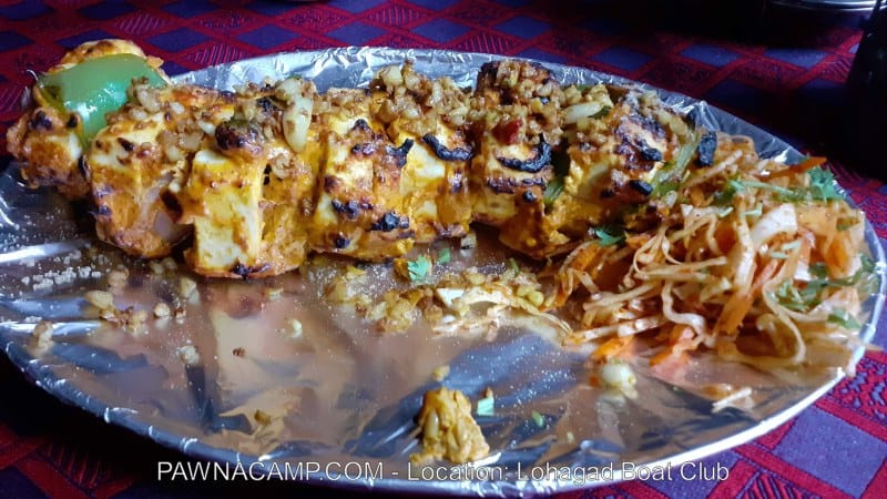 Grilled paneer skewers topped with spices and served with a side of salad on a silver platter.