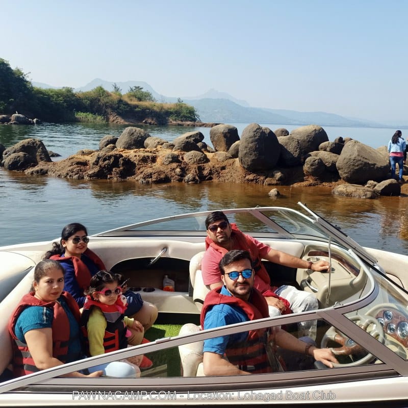 Four individuals wearing life jackets seated in a boat on Pawna Lake, with rocky formations in the background.