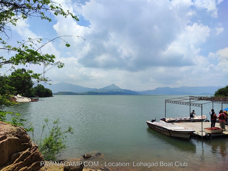 A view of the boating area at Pawna Lake with a dock and boats near the shore under a cloudy sky.