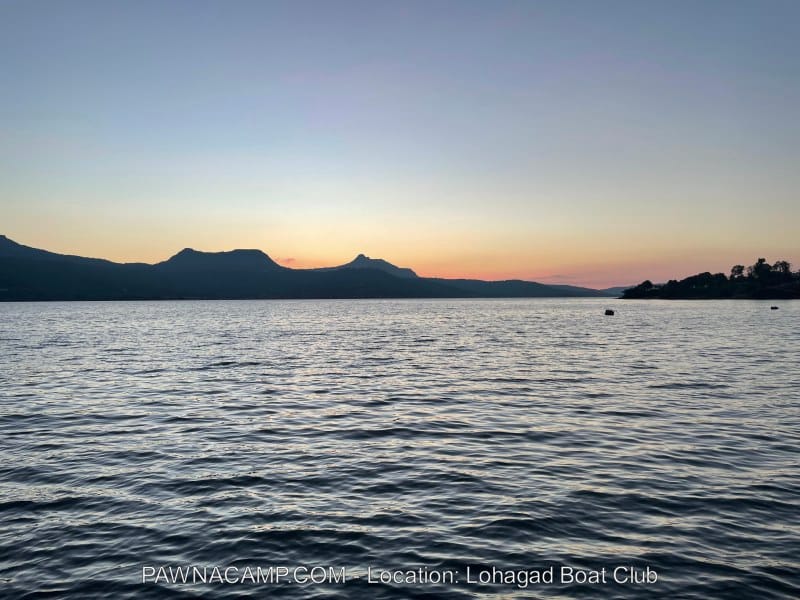View of Pawna Lake at sunset with mountains in the background and water reflecting the evening sky.