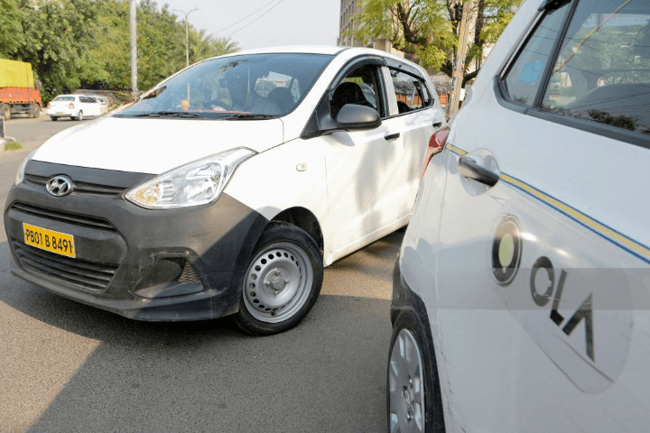 A car, possibly an Ola cab, parked on a street, suggesting a journey to a Pawna lake stay.
