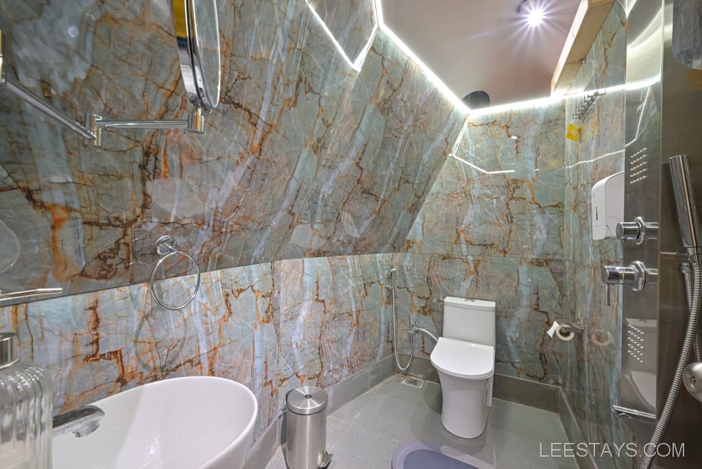 Luxurious bathroom at Domestory Resort, Malvandi Lake, featuring marble walls, modern fixtures, a white toilet, and a sink, creating an elegant and sophisticated ambiance.